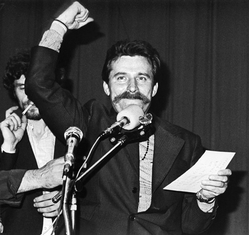 lech walesa black and white standing speaking microphone fist in air holding notes