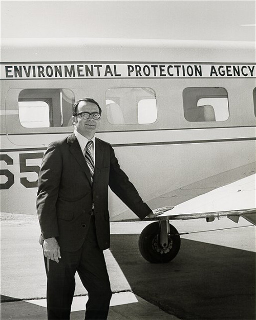 william ruckelshaus standing black and white outside small plane via servetolead.com