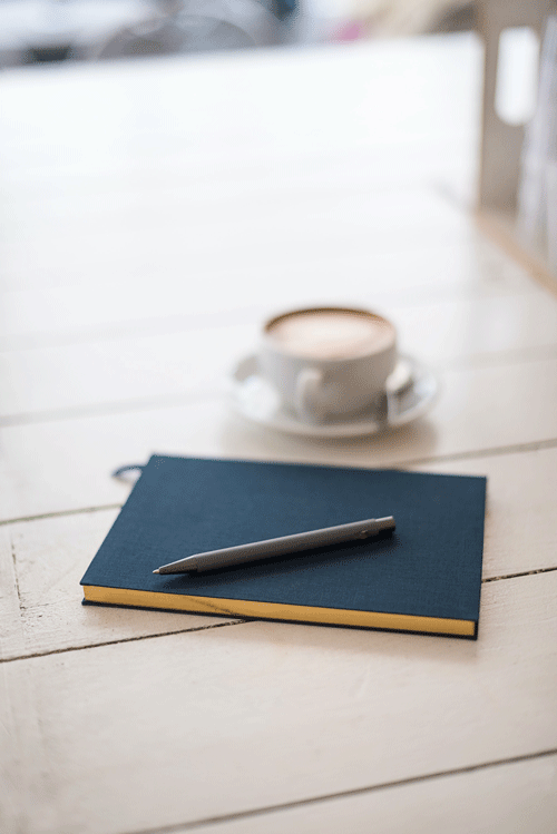 color photograph of blue book and pen on white table near coffee